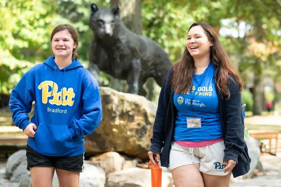 Two students walking in front of the panther statue in the quad