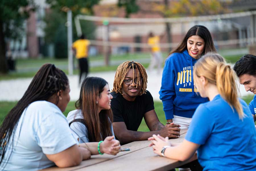 Students talking at a picnic table in front of a fire pit.