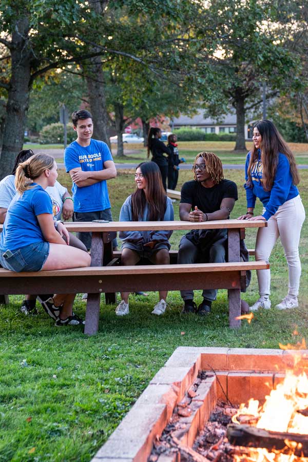 students at a bonfire talking at a picnic table