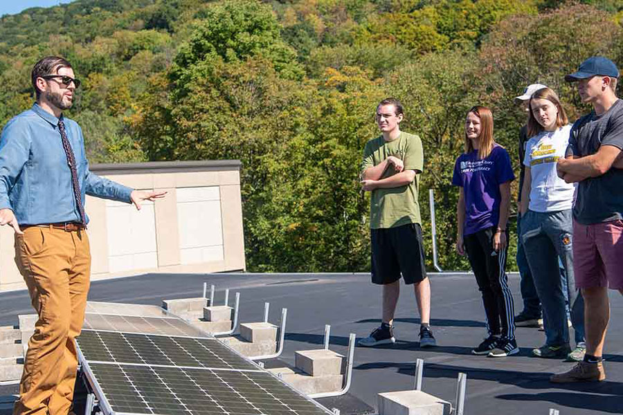 Students and professor talking on a roof with solar panels