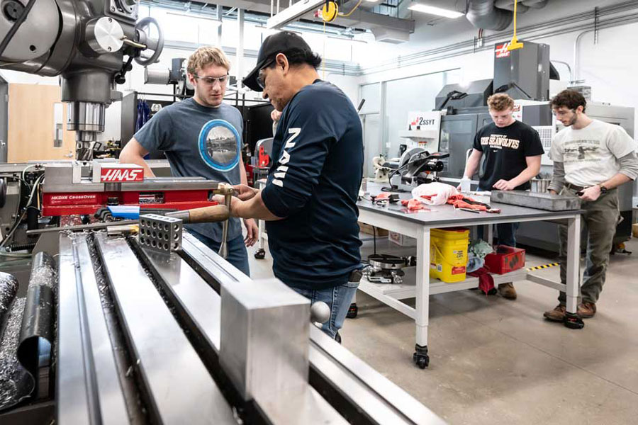 Professor and students standing in front of a drill press