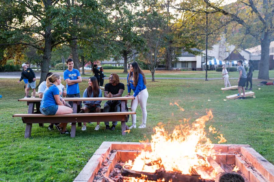 Group of studentat picnic table with a bonfire in the foreground