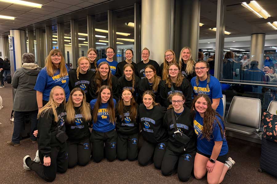 Women's softball team smiling in a group picture at the airport