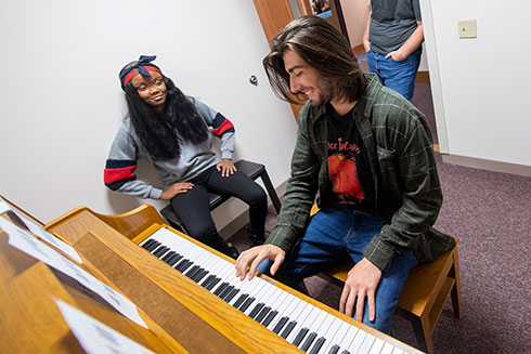 A male and female student at a piano in a practice room