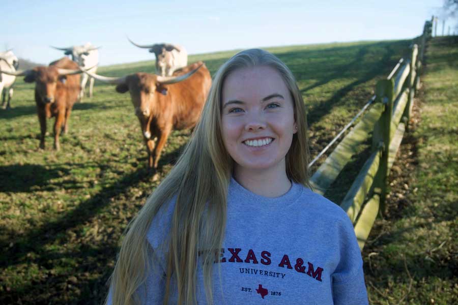 Zoe Halpate showing she is going to Texas A&M in front of a field of longhorn cows