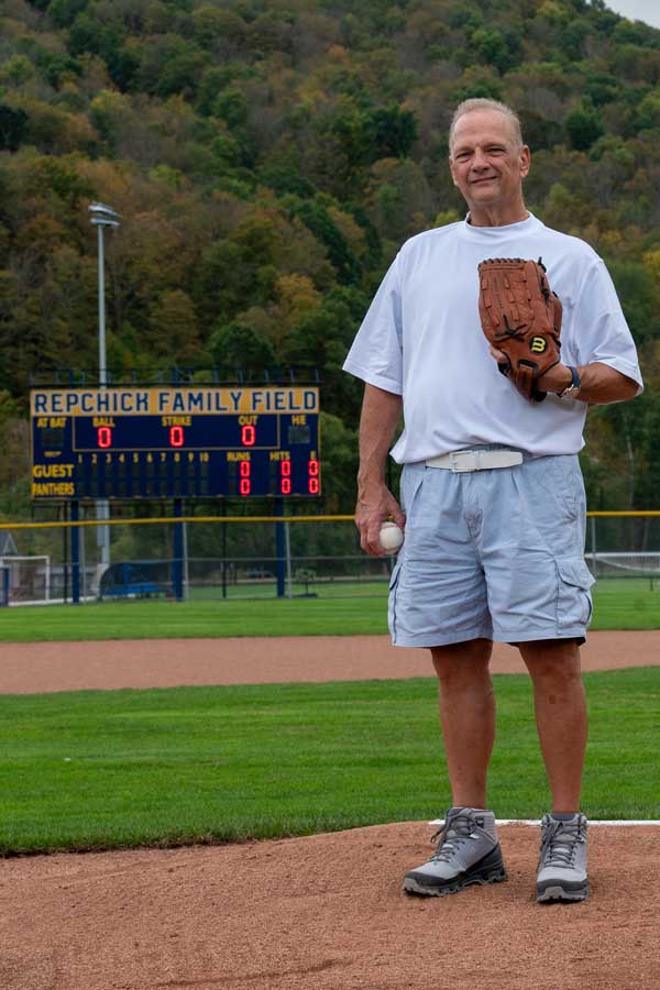 George Repchick standing at the pitcher's mound with the dedicated scoreboard behind him