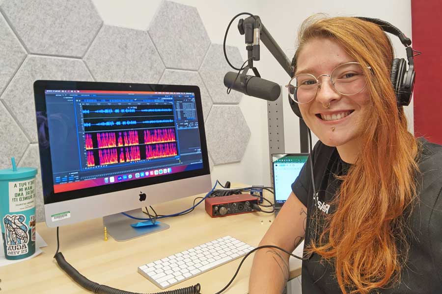 Hayley sitting at a desk with a omputer screen and microphone.