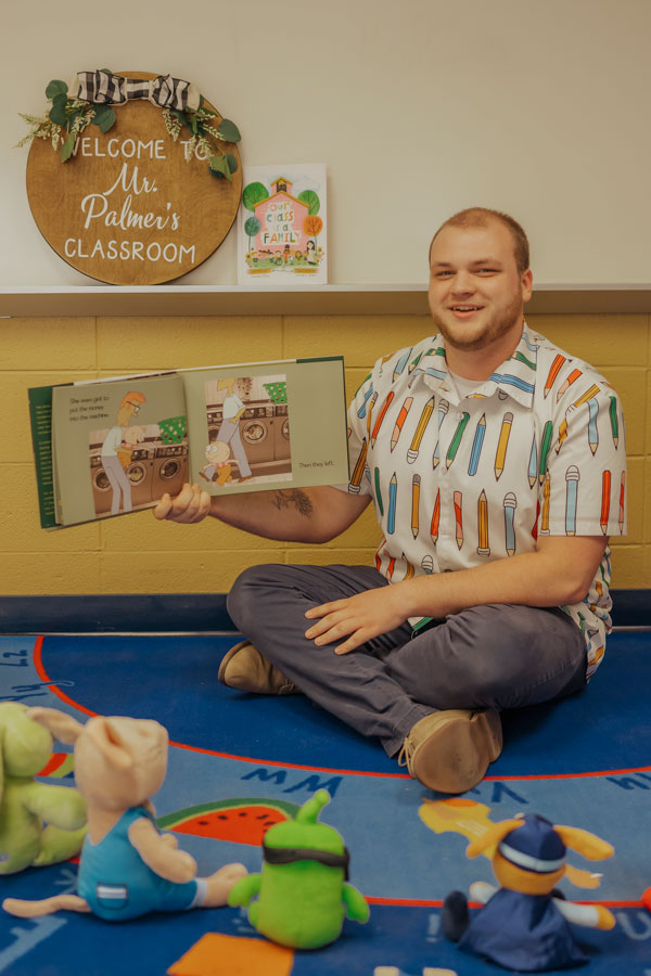 Cole reading holding a bok with stuffed animals in the foreground