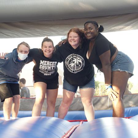 Four students in shorts bend over for a photo in an air-filled bounce castle